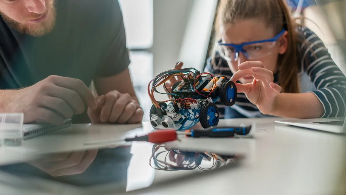 En ung elev och hennes lärare studerar en robot.