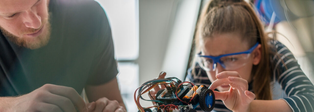 En ung elev och hennes lärare studerar en robot.
