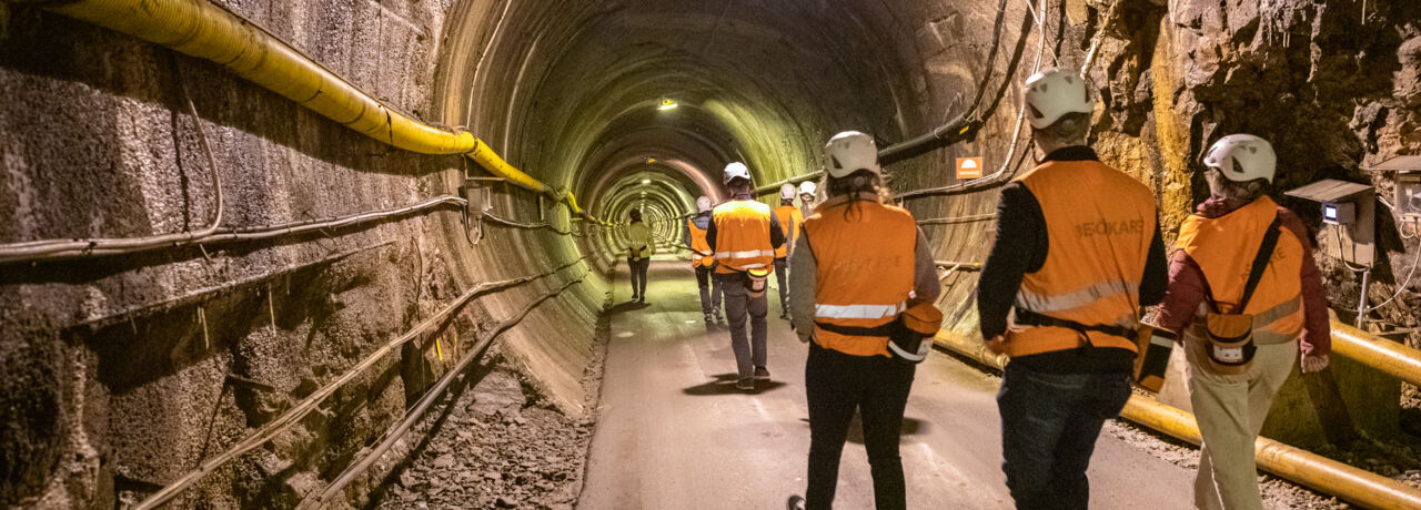 Personer i tunnel med hjälmar och orange västar.