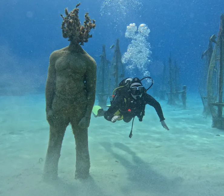 A diver under water next to a statue