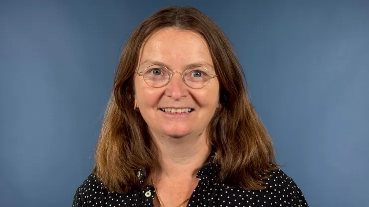 Porträtt av person med mellanlångt brunt hår framför en blå bakgrund.