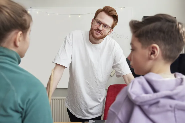 Manlig lärare står framför två elever i klassrum.