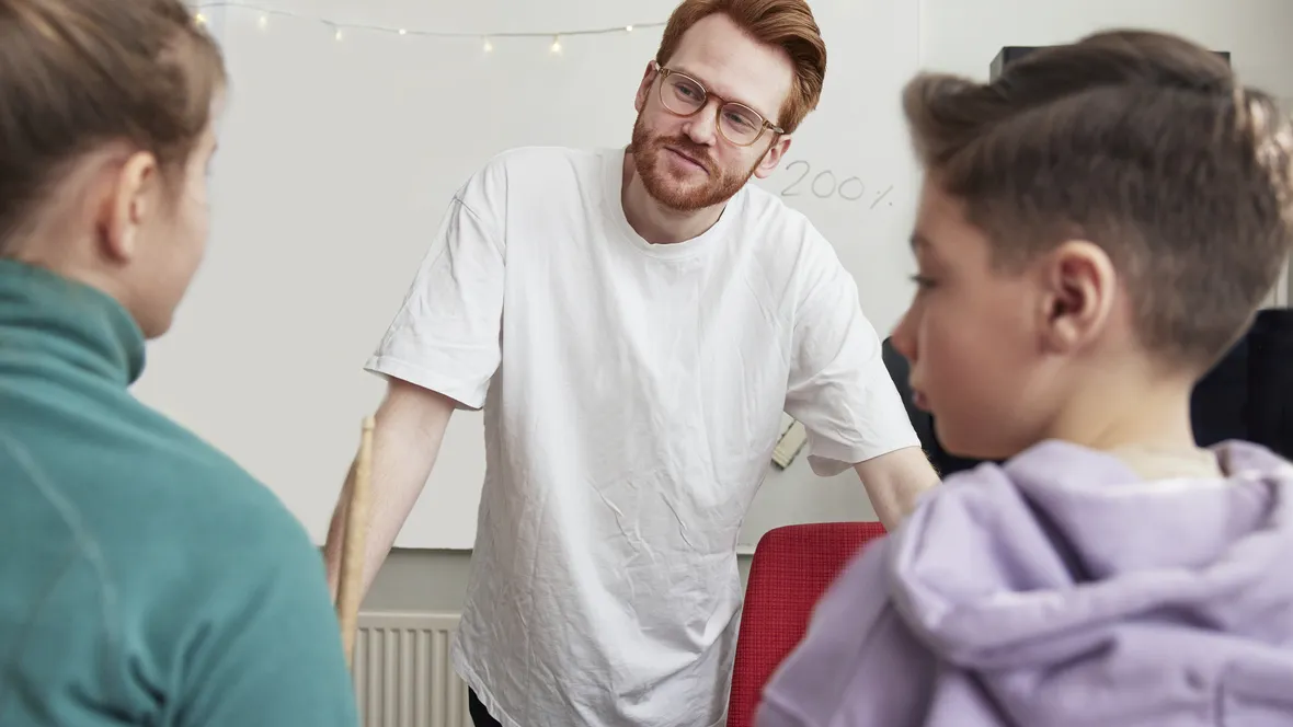Manlig lärare står framför två elever i klassrum.
