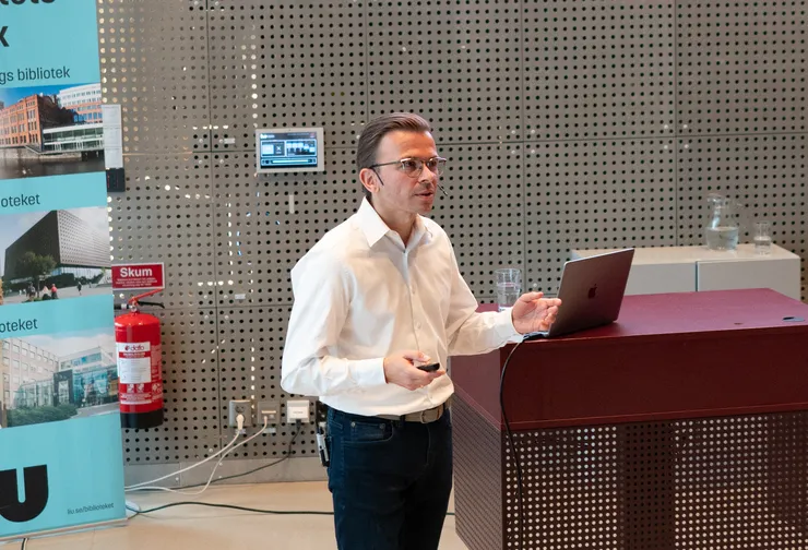 En man håller en presentation för en publik av människor som lyssnar uppmärksamt.