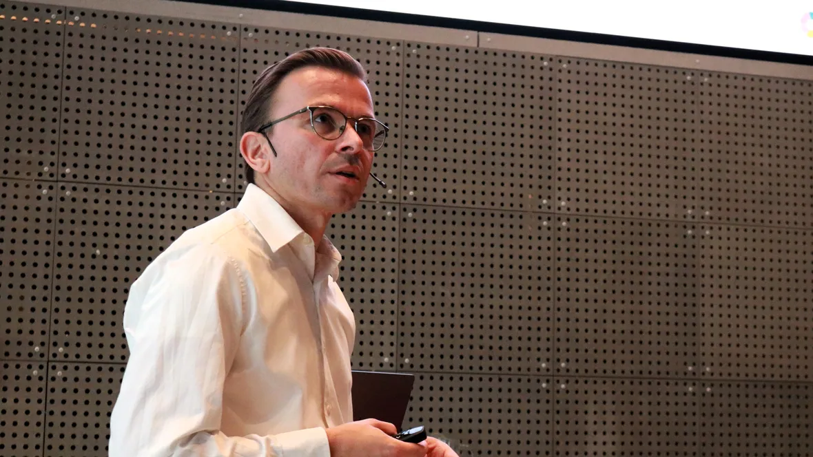 A man delivering a presentation to an attentive crowd, highlighting key points with gestures.