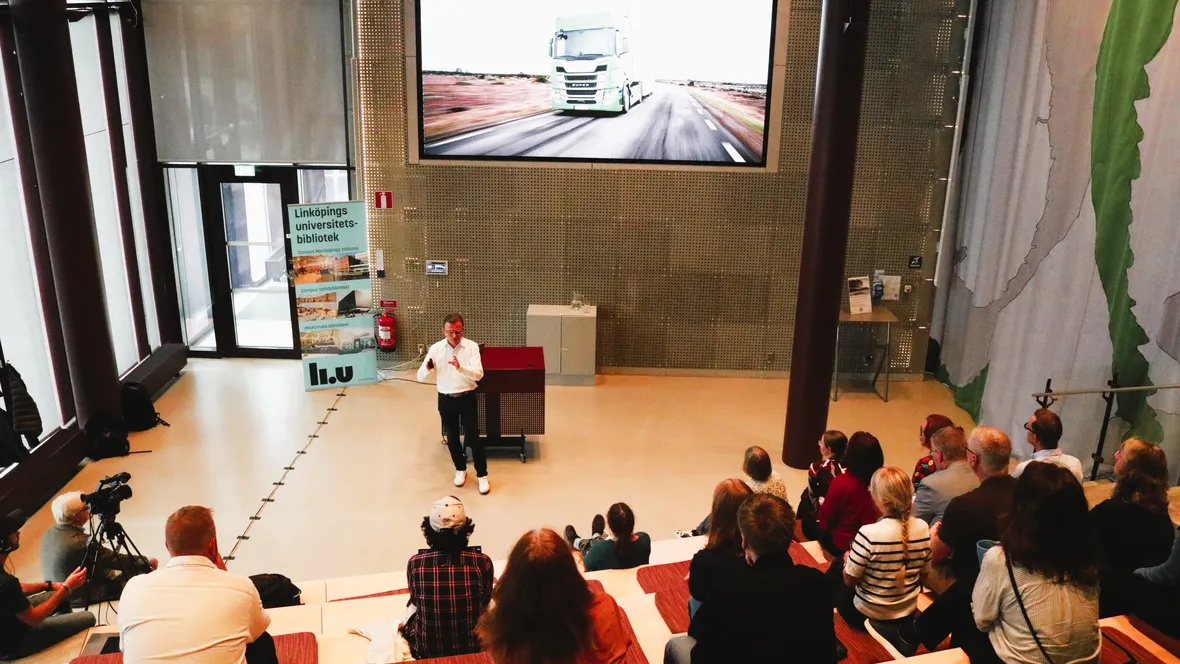 A man delivering a presentation to an attentive crowd, highlighting key points with gestures.