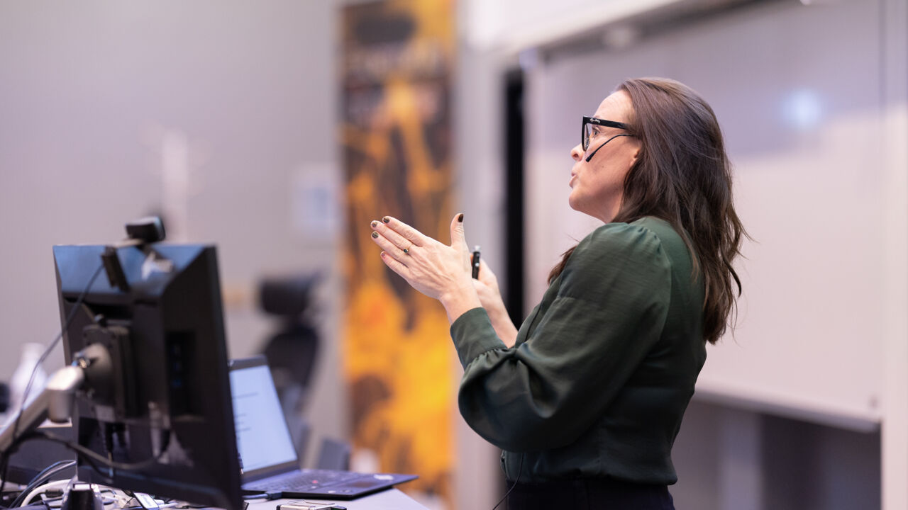 Woman lecturing in front of a whiteboard.