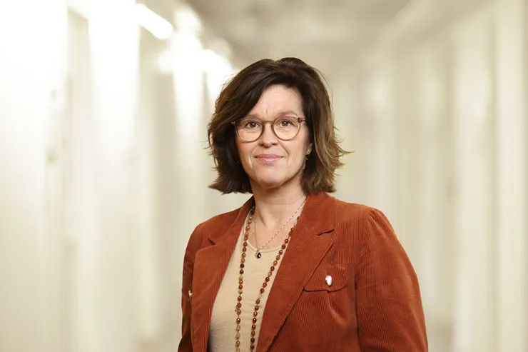 Porträtt av en kvinna med brunt hår och orange kavaj