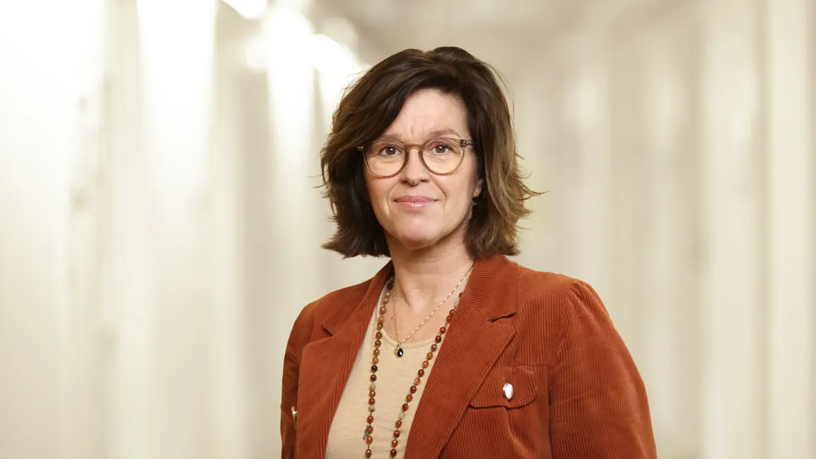 Porträtt av en kvinna med brunt hår och orange kavaj