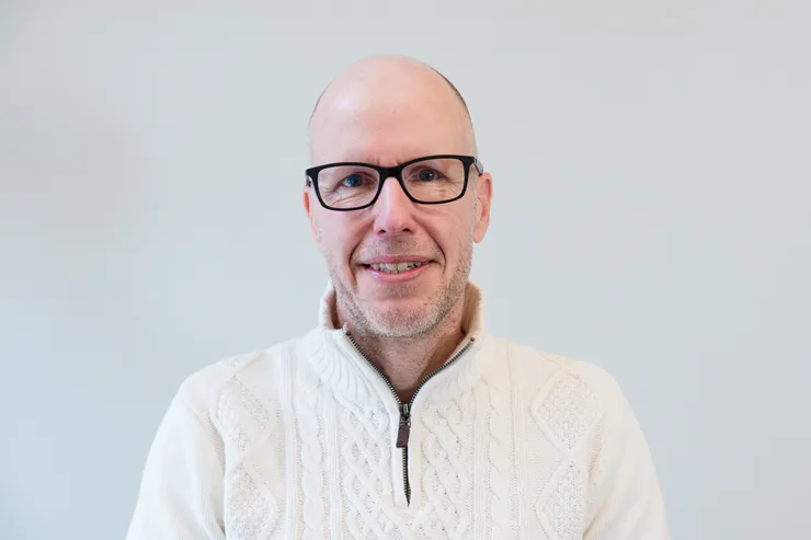Person med vit polotröja tittar in i kameran.