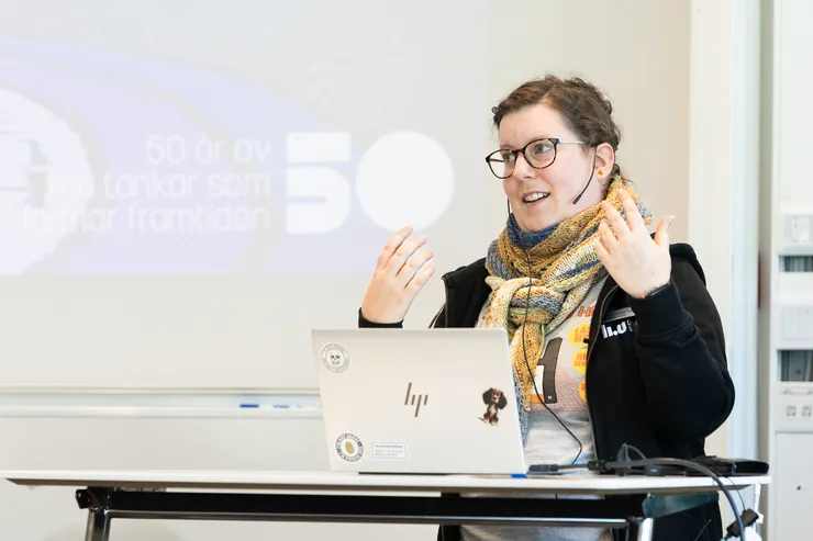 Person står framför projektorduk i ett klassrum och presenterar.