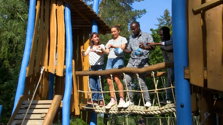 Four people standing on a rope bridge holding footballs.