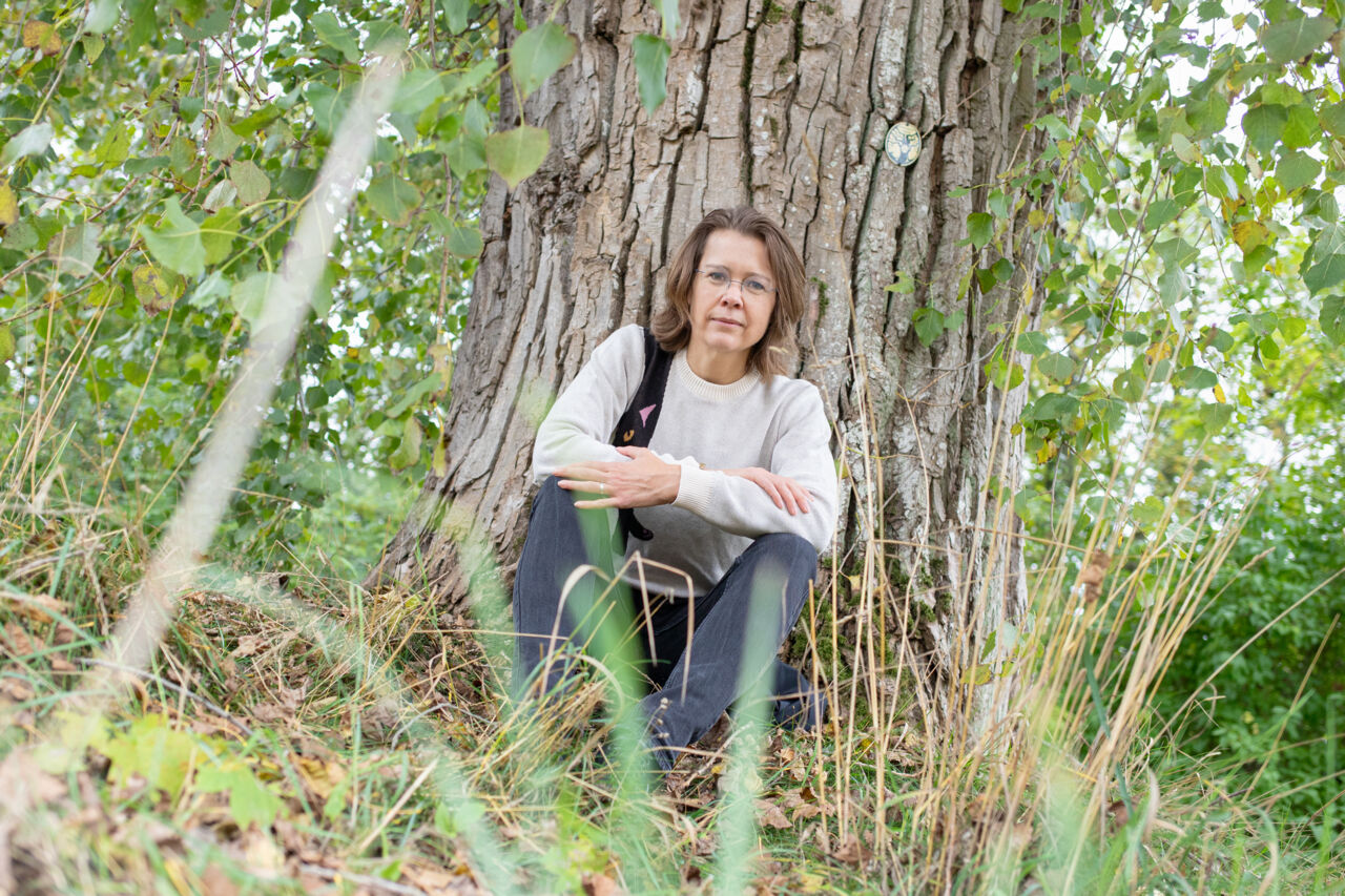 Kvinna vid ett träd tittar in i kameran.