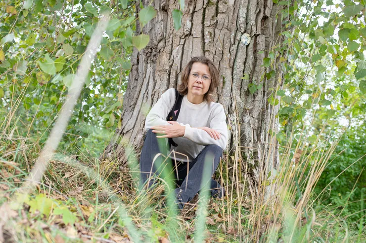 Woman by a tree looking into the camera.