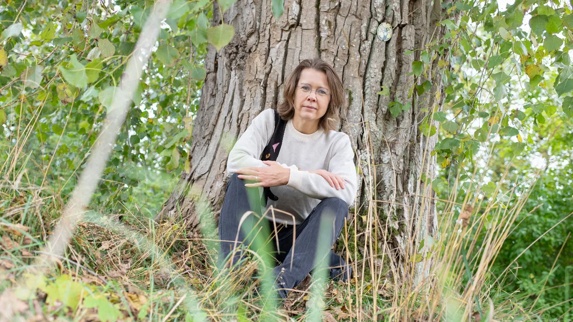 Kvinna vid ett träd tittar in i kameran.