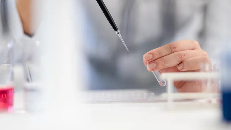 Pipett närmar sig hand som håller provrör.