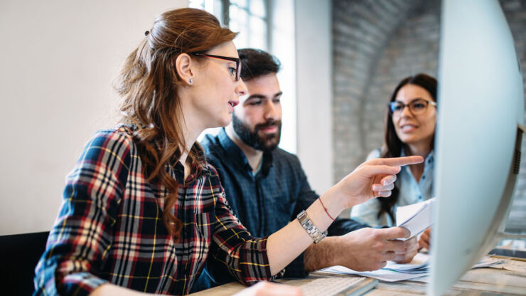 tre unga personer sitter framför en datorskärm och diskuterar