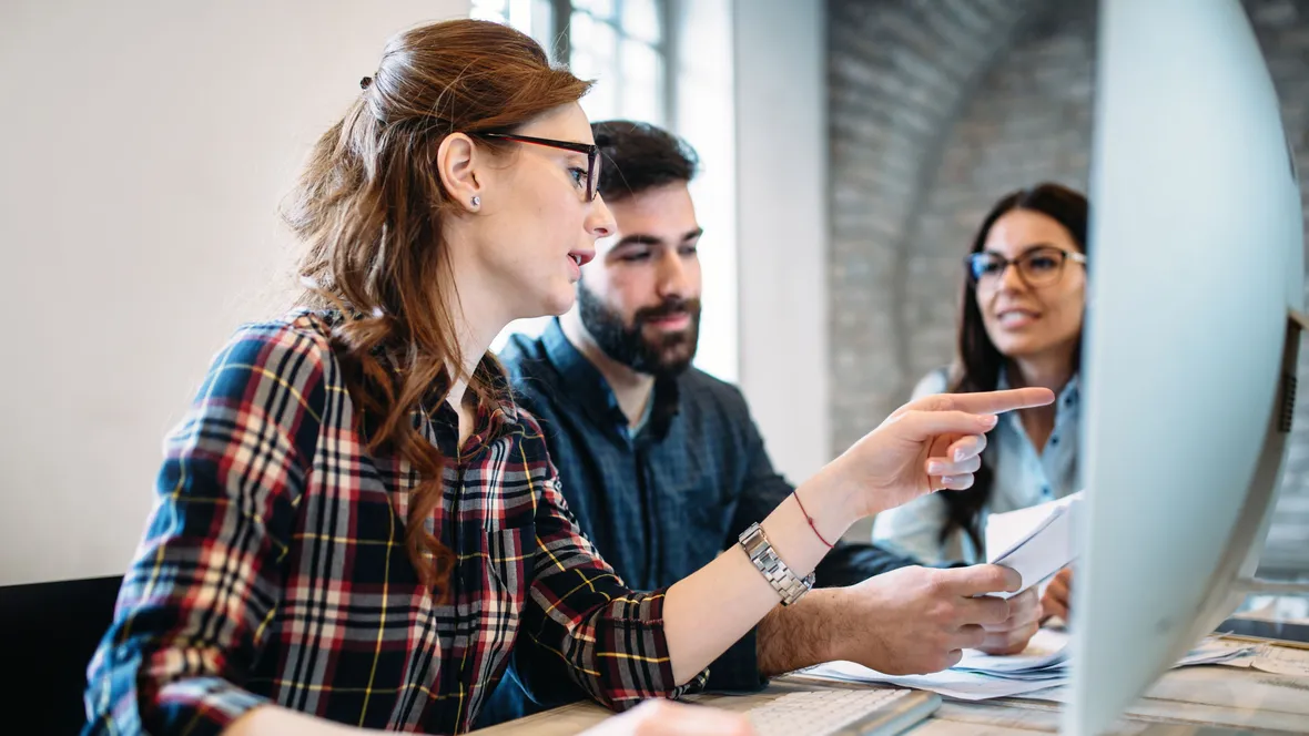 three young persons discussing while sat in front of a computer screen 