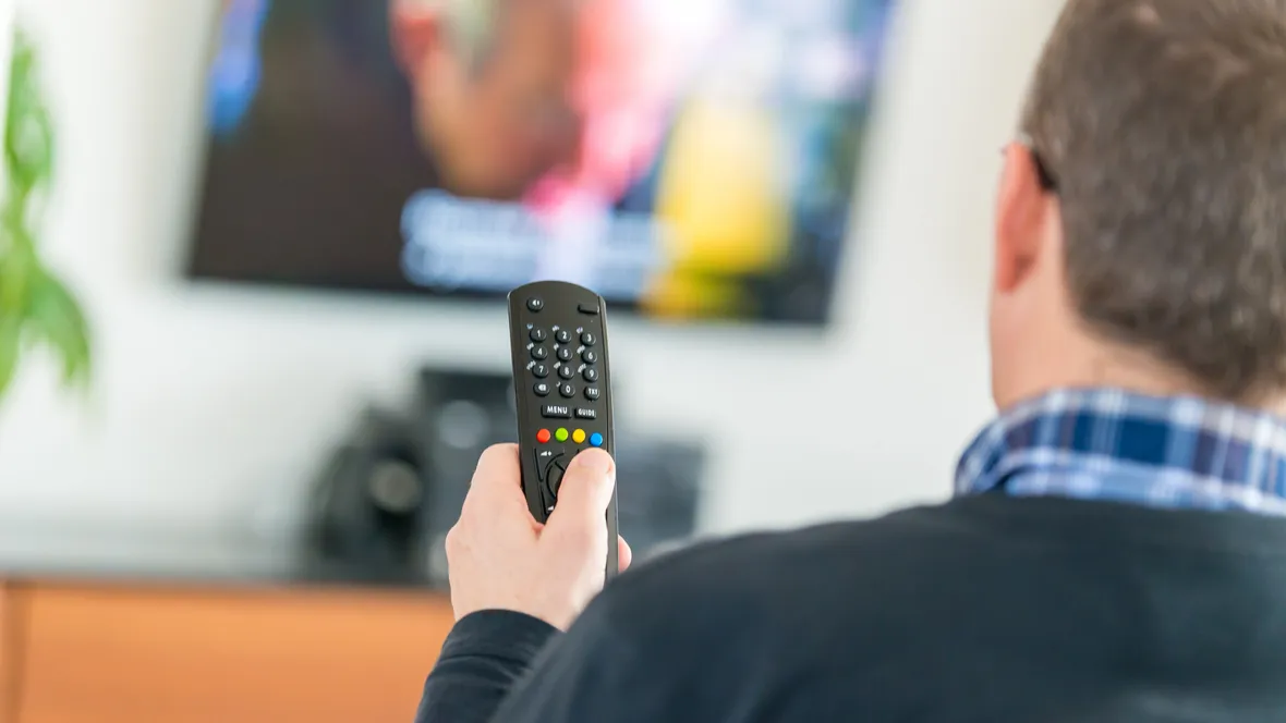 En man sitter framför en tv och håller en fjärrkontroll i handen.