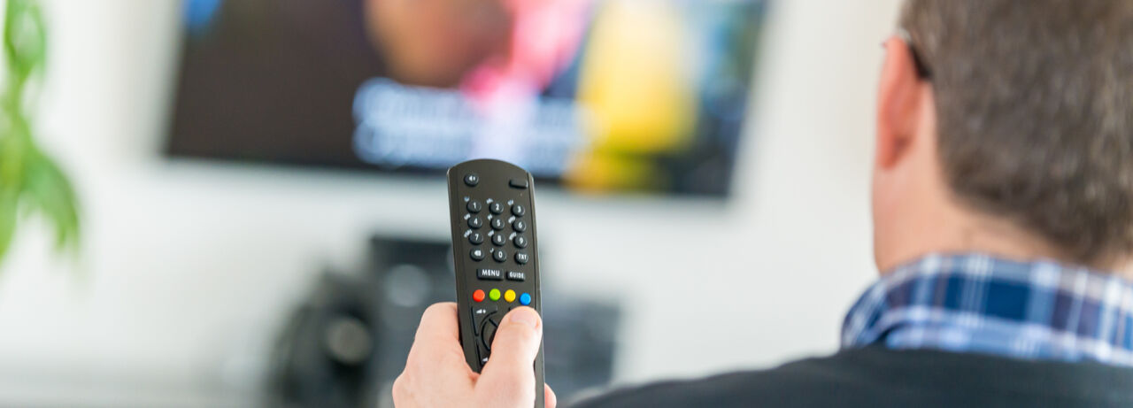 A man is sitting in front of a television holding a remote control in his hand.
