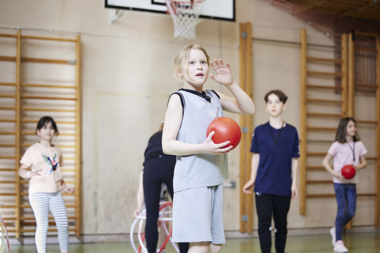 En grupp elever leker med en boll i en idrottshall.