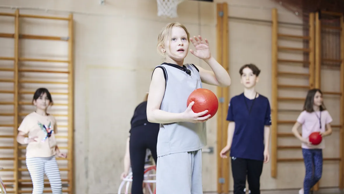 En grupp elever leker med en boll i en idrottshall.