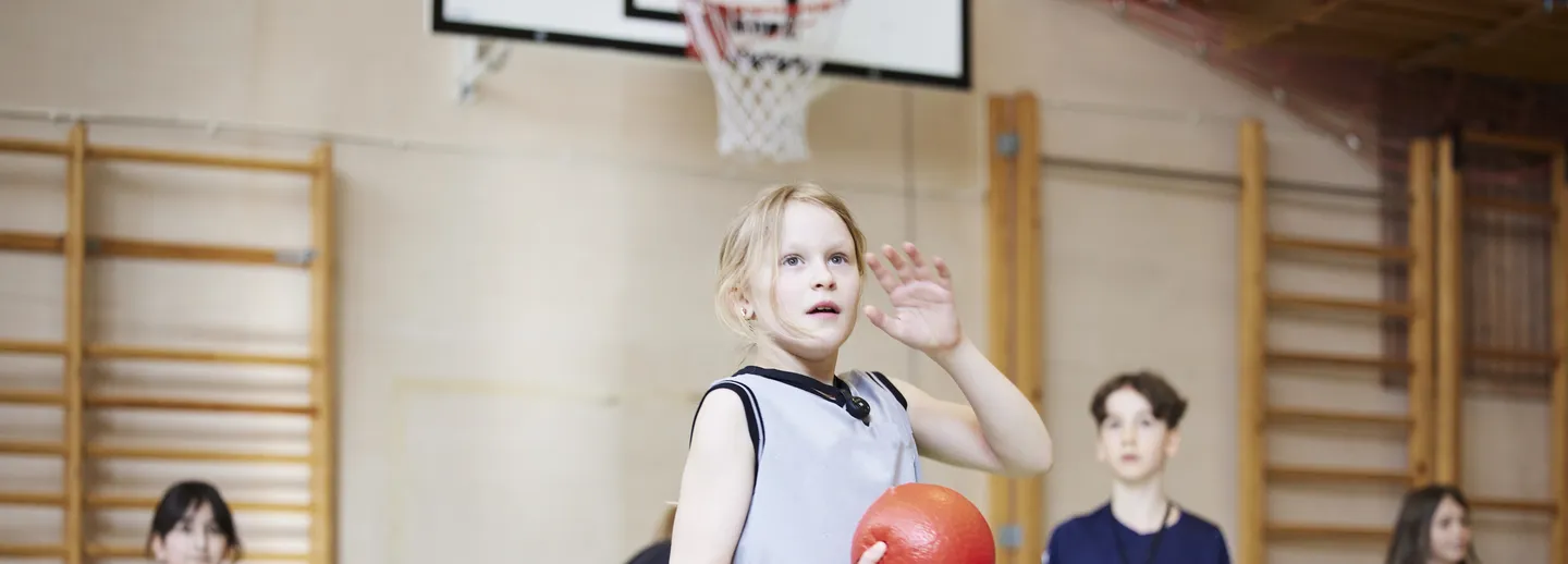 En grupp elever leker med en boll i en idrottshall.