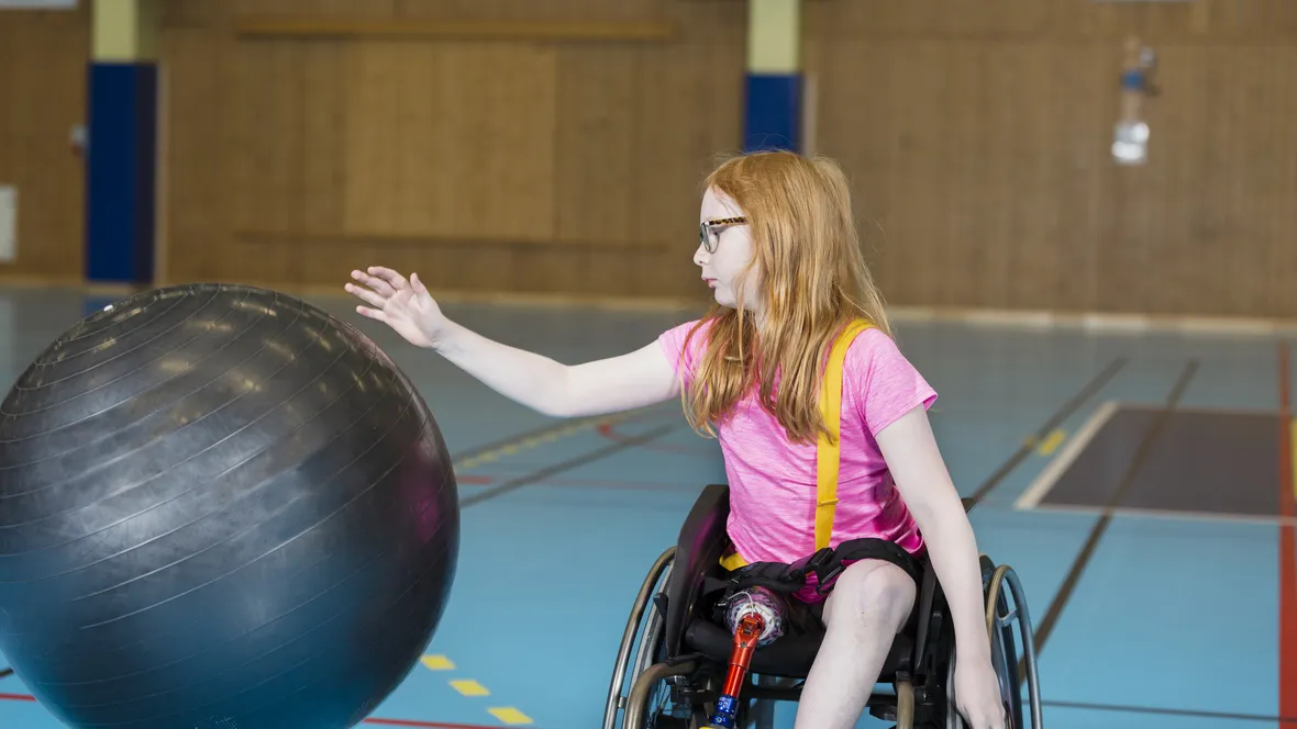 En flicka i rullstol som leker med en boll.