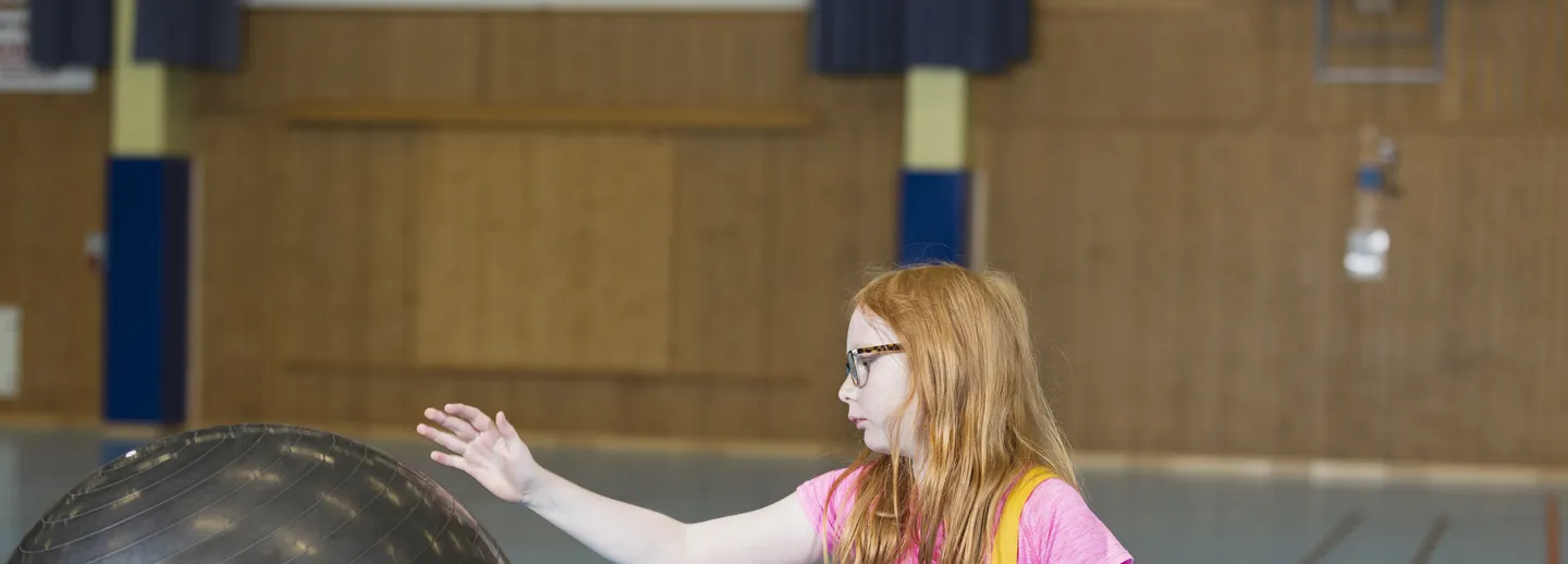 En flicka i rullstol som leker med en boll.