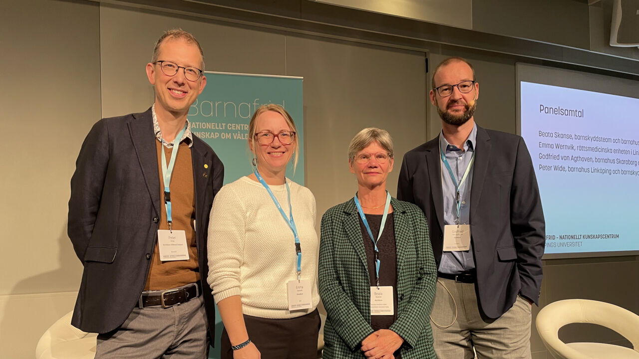 Två män och två kvinnor på rad som står i strålkastarljus i ett konferensrum.