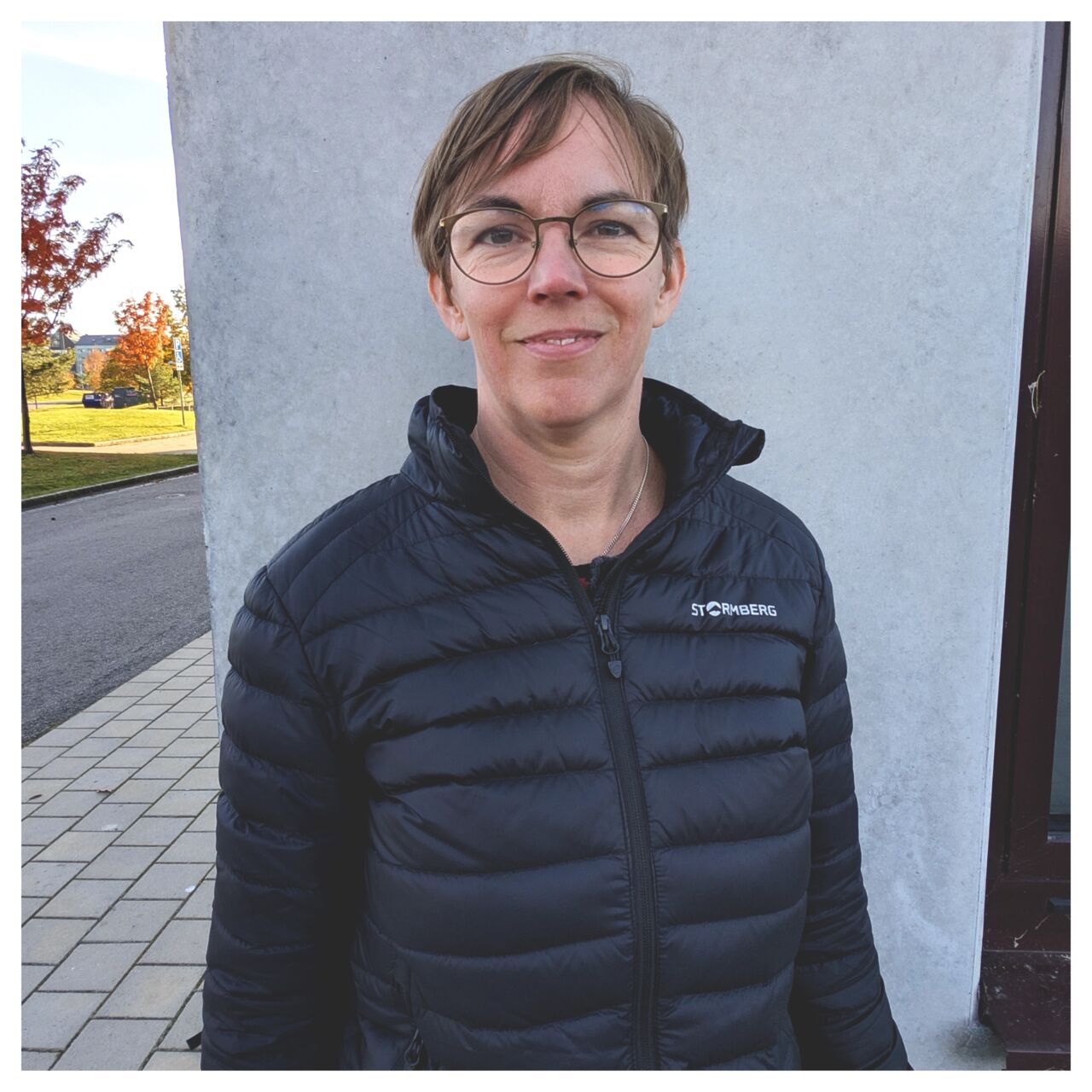 Avsnittsgästen Karin Stolpe står utomhus lutad mot Studenthuset på Campus Valla.