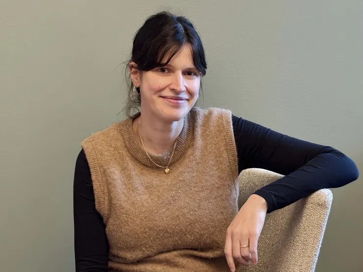 Porträtt på leende kvinna framför en grön vägg.