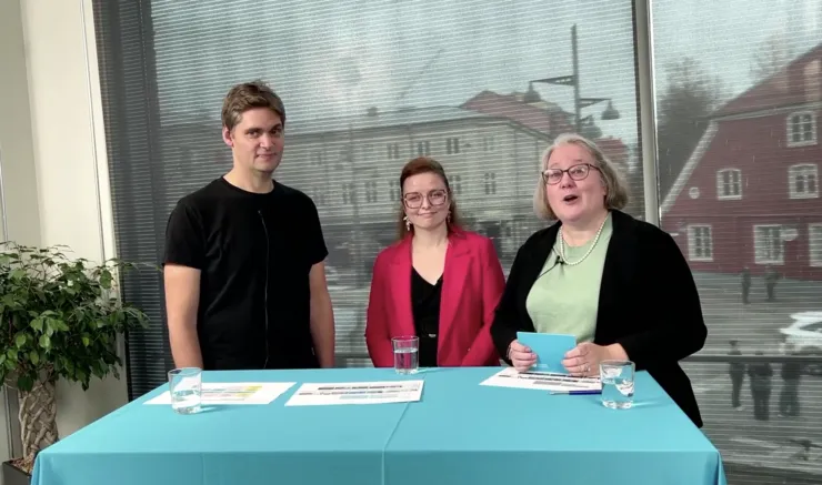 Three people behind a table, holding a webinar