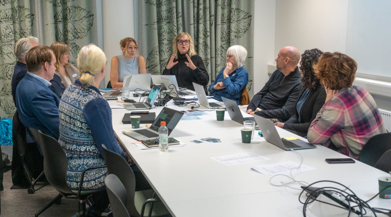 Deltagare sitter vid ett bord och följer konferensen via skärm.