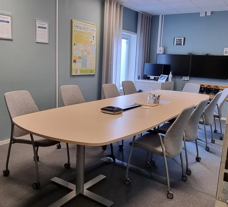 Mötesrum med avlångt bord, flera stolar och stora bildskärmar.
