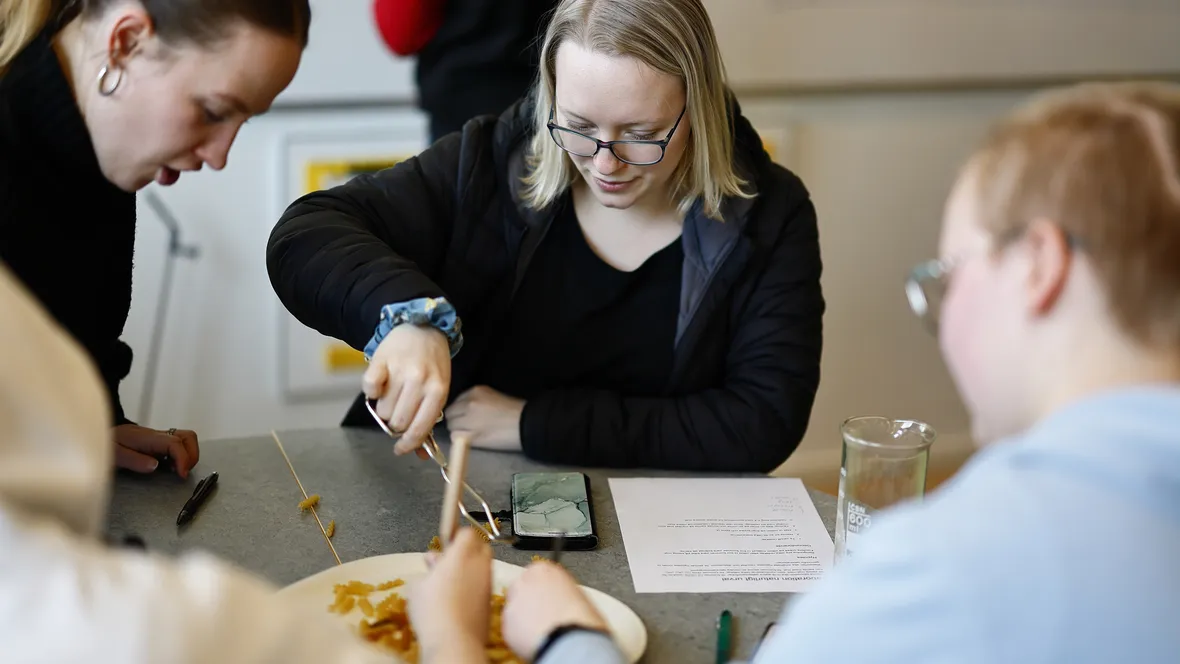 Tre elever på gymnasiet pratar och laborerar vid bord.