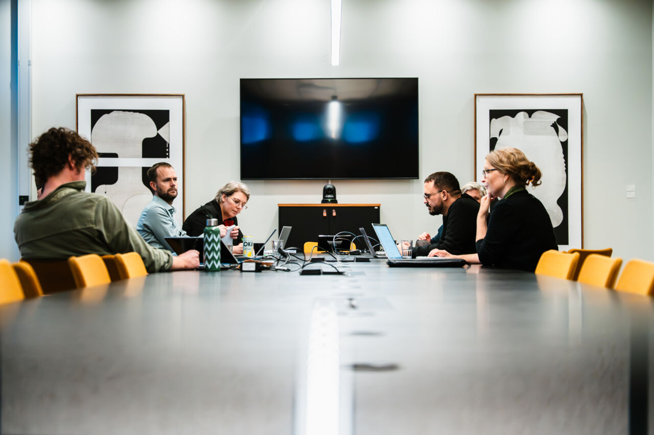 Personer sitter runt ett konferensbord i ett modernt mötesrum och diskuterar under CMHB:s Visionary Day. En stor skärm syns i bakgrunden.