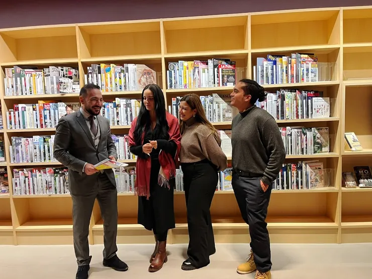 Four persons standing in front of a large cabinet filled with newspapers and magazines.