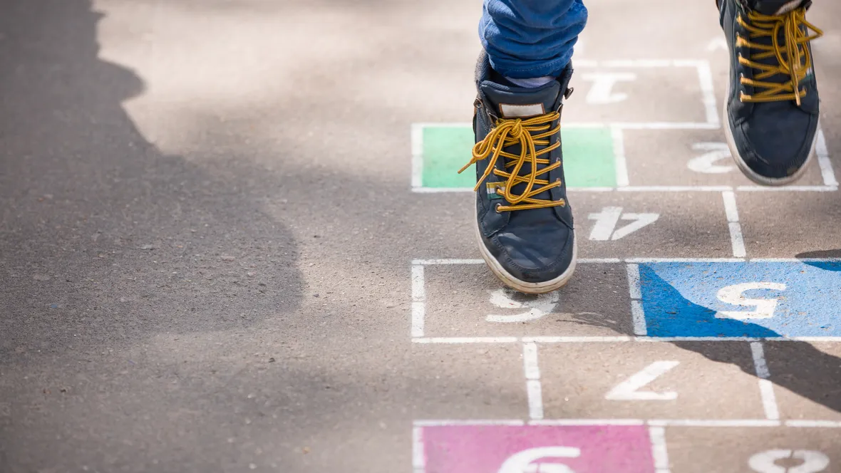 Ett barn leker hoppa hage på lekplatsen utomhus en solig dag.