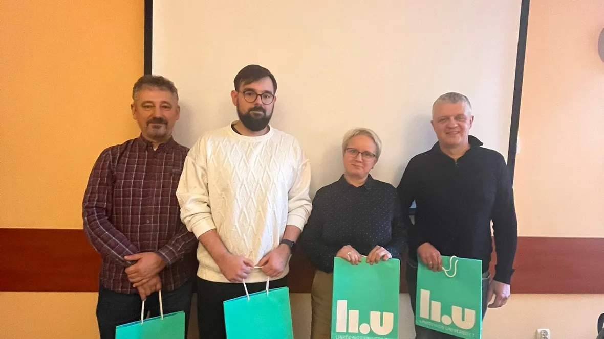 Four people standing in front of a screen and holding one green paper bag each