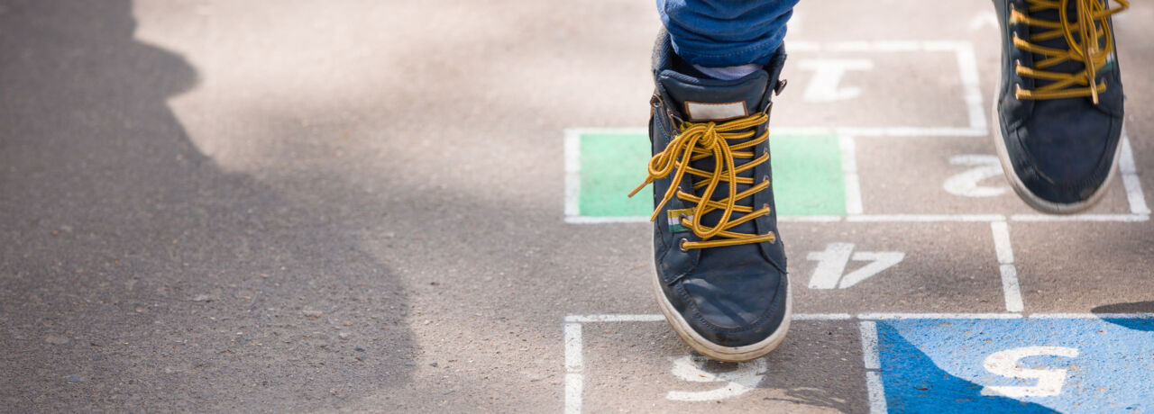 Ett barn leker hoppa hage på lekplatsen utomhus en solig dag.