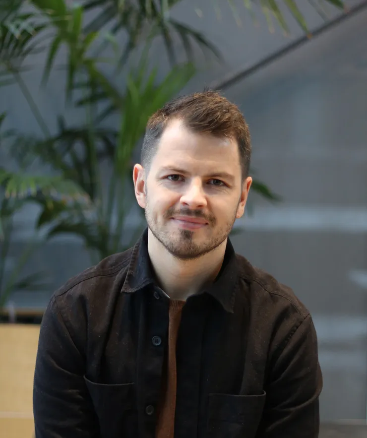 Porträttbild på leende man framför en grän växt.