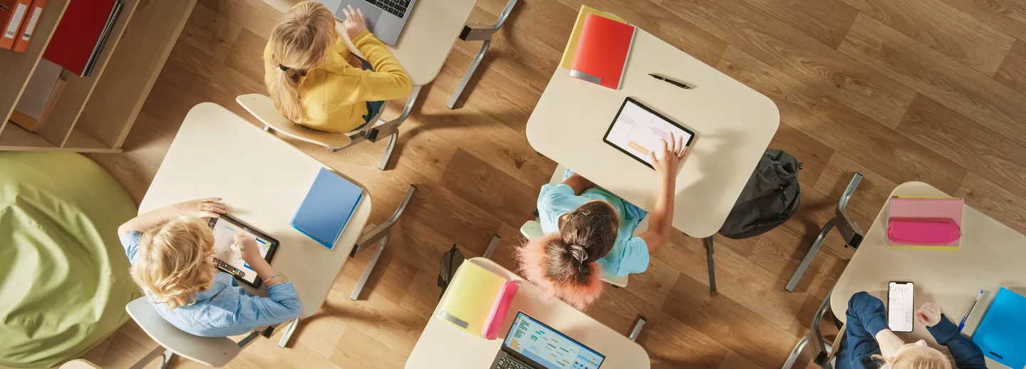 Bilden visar elever sittande vid sina skolbänkar, fotograferade uppifrån.