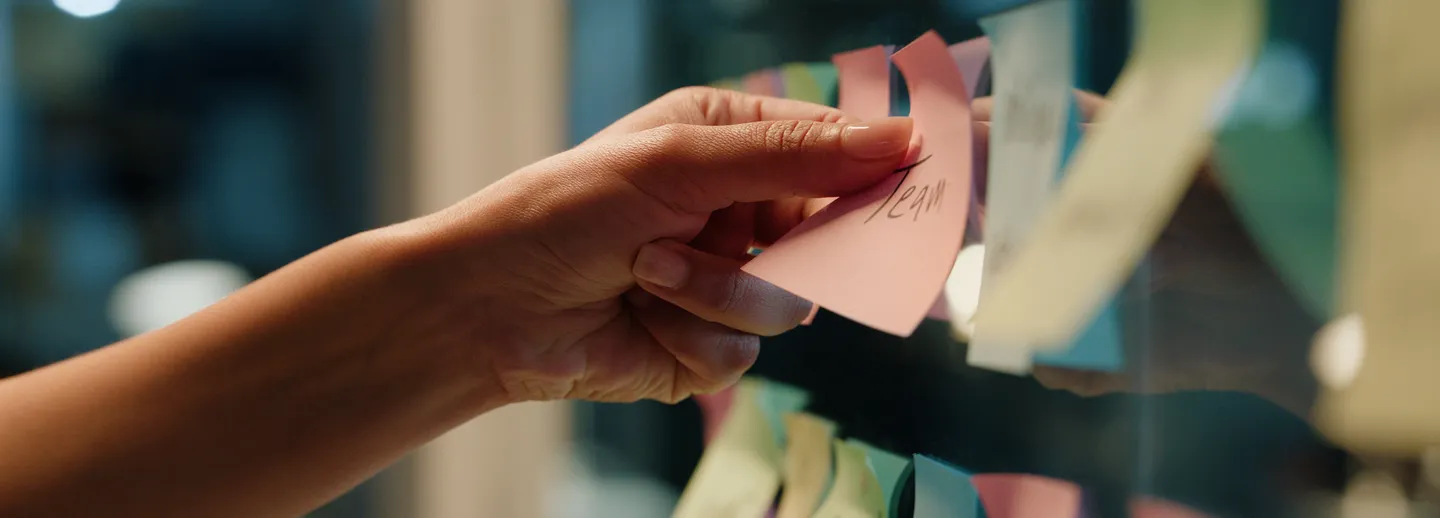 En hand sätter upp lappar med anteckningar på en vägg under en workshop.