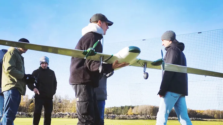 Studenter utomhus, håller en drönare, flygplan.
