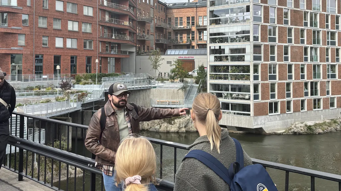 En man står utomhus på en bro och talar inför flera personer.