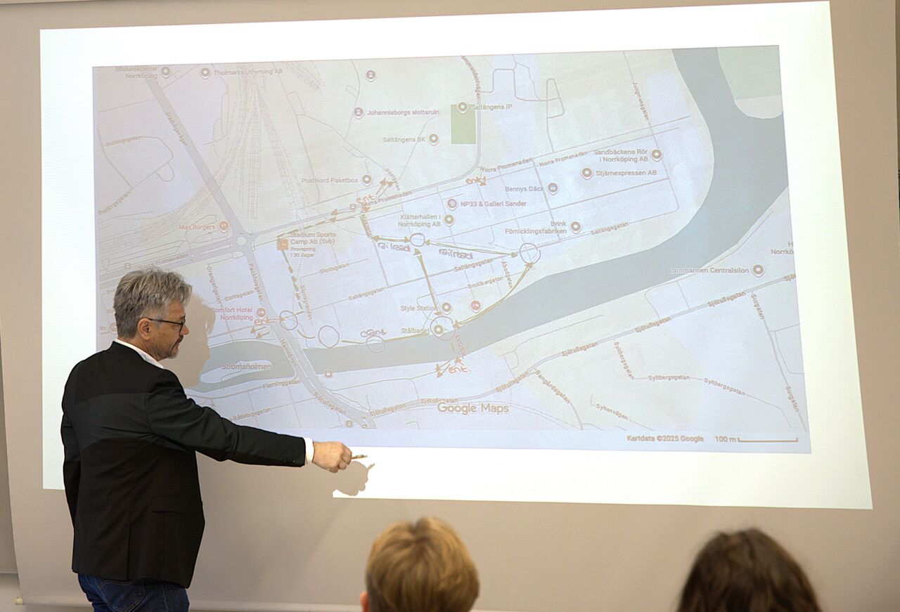 Man står i en lärosal vid en filmduk och pekar på en karta. 