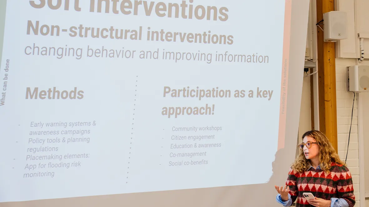A person is standing in a lecture hall by a projection screen.
