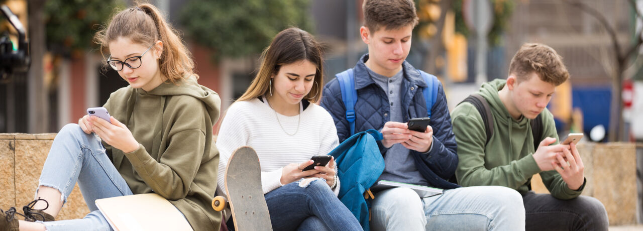 Tonåringar sitter på bänk och tittar i mobiler.
