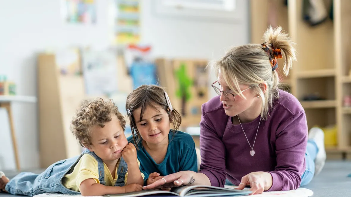 Lärare och barn ligger på golvet och läser en bok tillsammans.